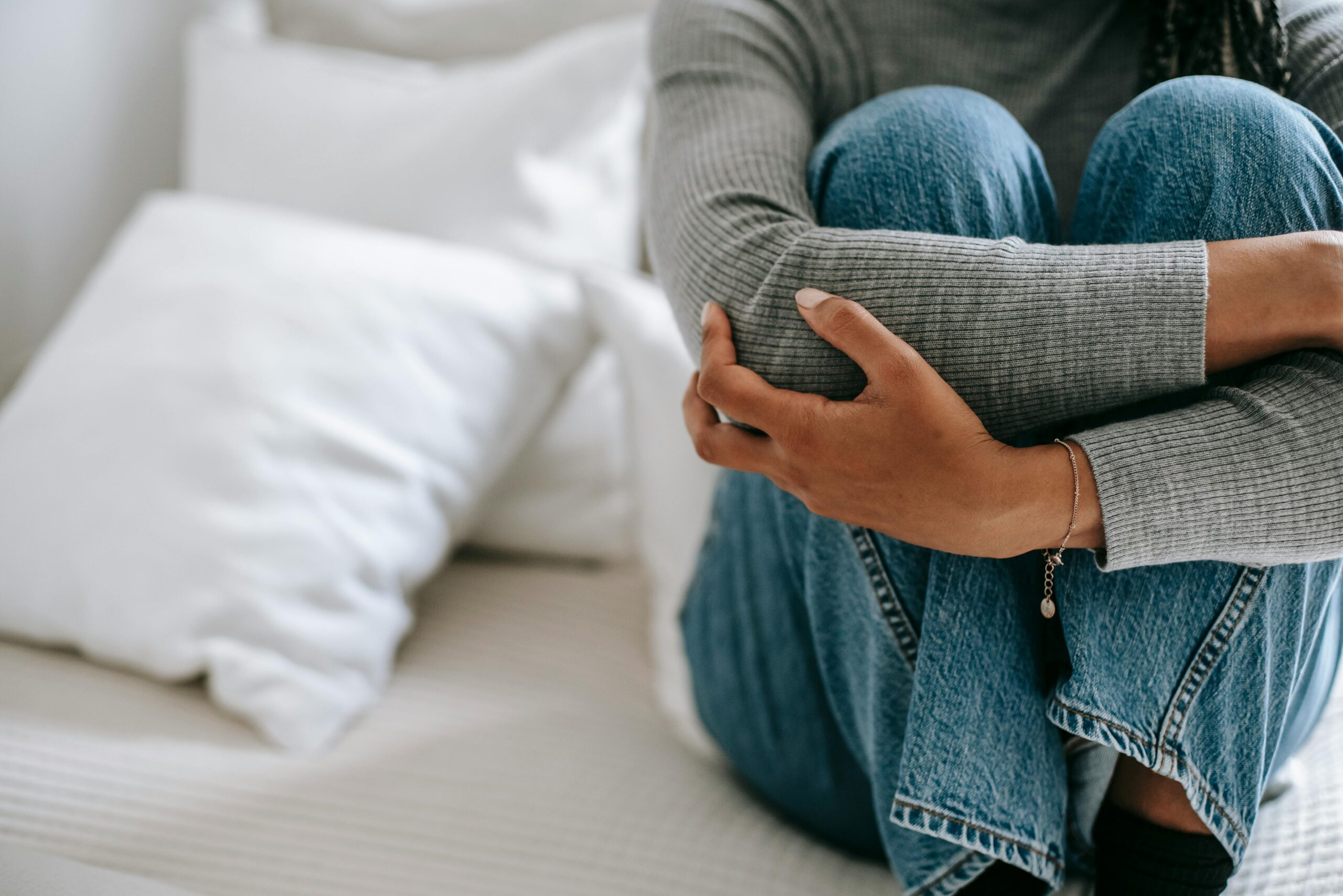 Image of an anxious young woman sitting on a bed embracing her knees in despair